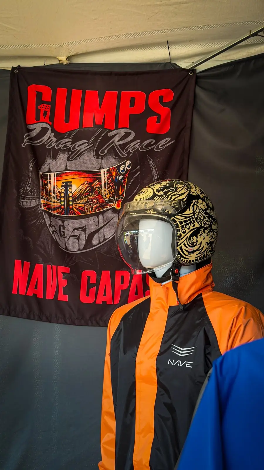 Manequim vestindo jaqueta laranja e azul e capacete dourado, montado em frente ao banner do Gumps Drag Race.