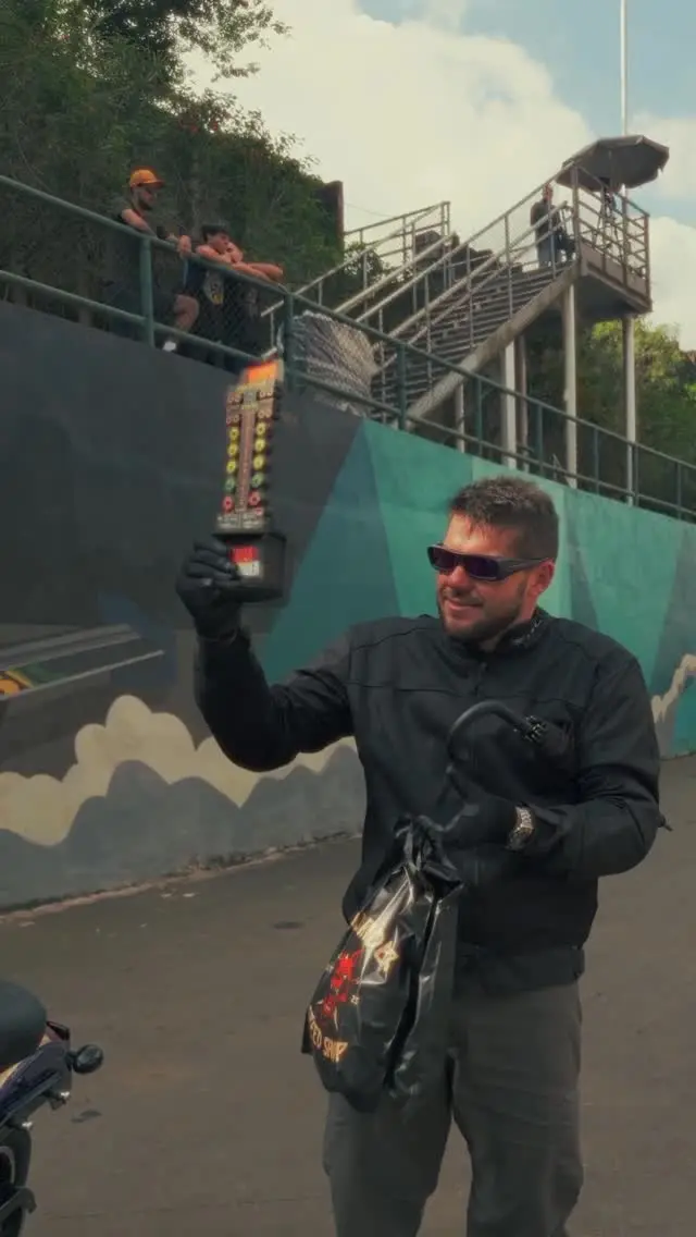 Piloto de jaqueta preta e óculos escuros levantando uma capa de moto na área dos boxes.