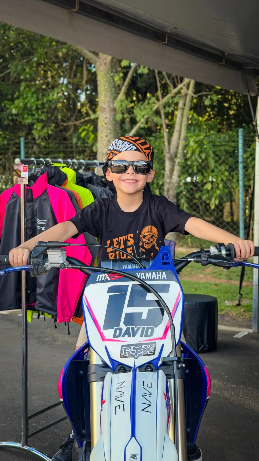 Menino sentado em uma moto de trilha com o número 15, embaixo da tenda do evento.