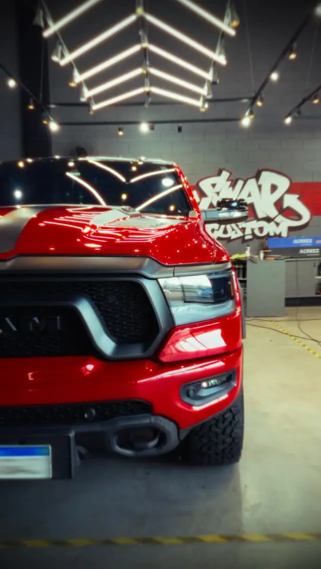 Dodge RAM vermelha polida, de frente, dentro de uma oficina com luzes de LED no teto.